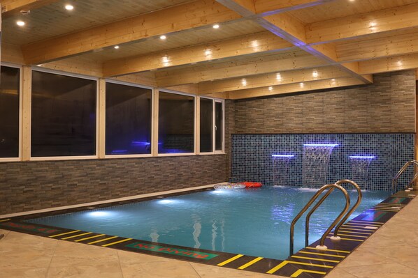 An indoor swimming pool with clear lane markings, a tiled wall with water features, and a wooden ceiling. - Marigold Sarovar Portico , Shimla. Heated pool & AC Rooms (Resort cottage and SPA) (Shimla)