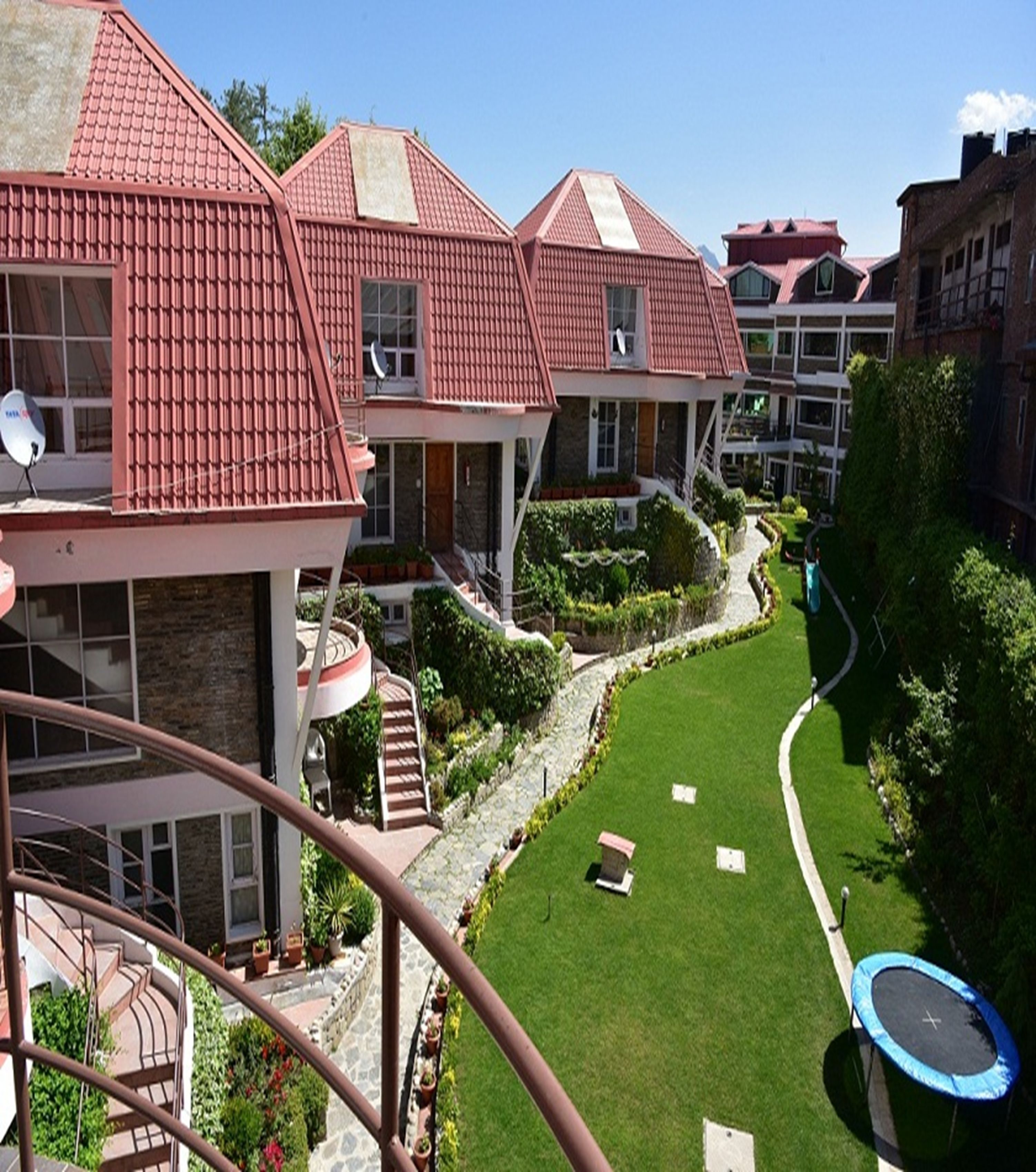 Un edificio residencial con varios tejados de tejas rojas, un césped bien cuidado y una escalera visible que lleva a los pisos superiores.