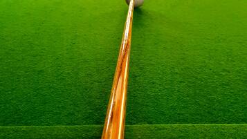 A close-up of a pool cue on a green felt pool table with a pocket of balls in the background.