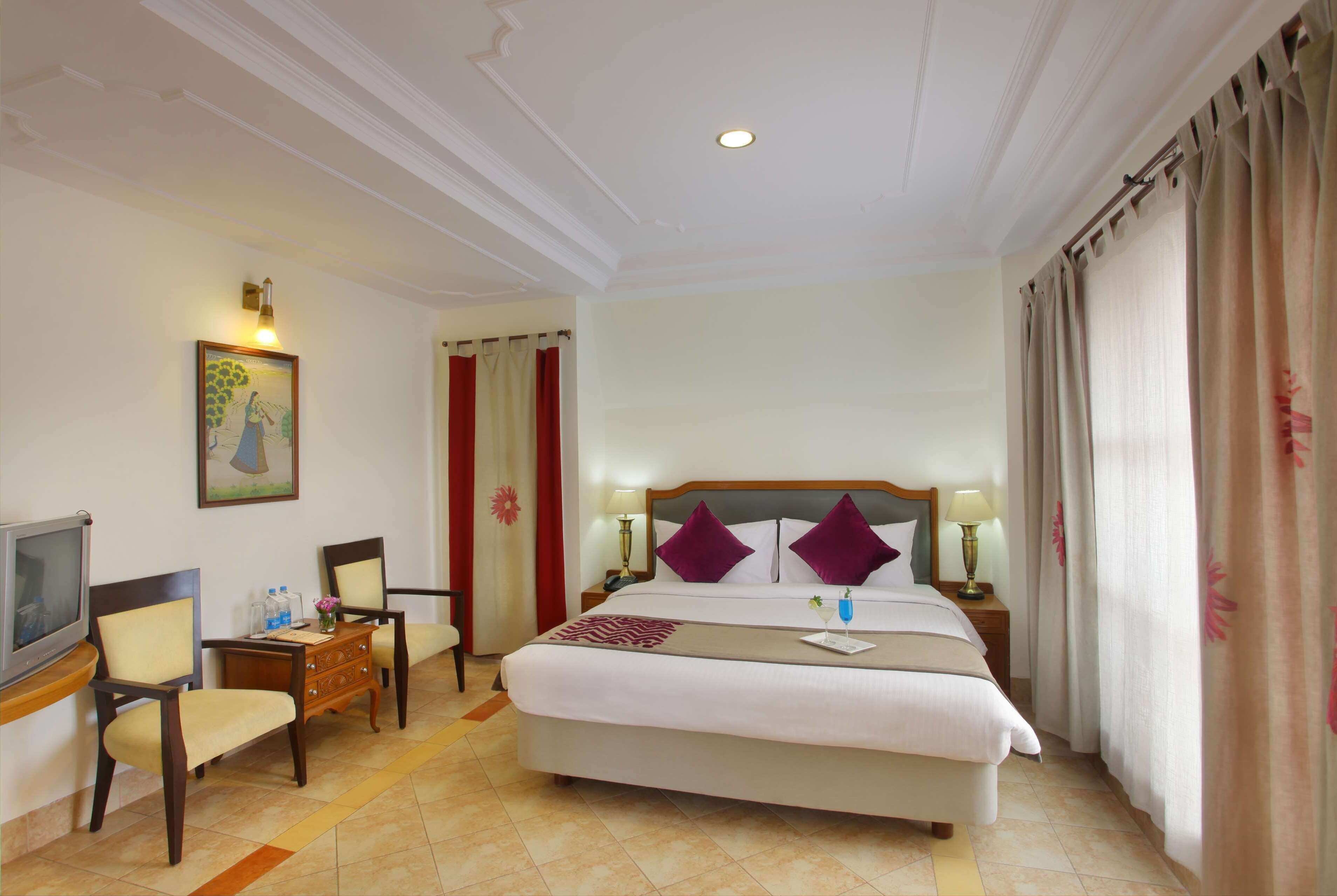Habitación de hotel con una cama, dos sillas, un escritorio, un televisor y un cuadro en la pared.