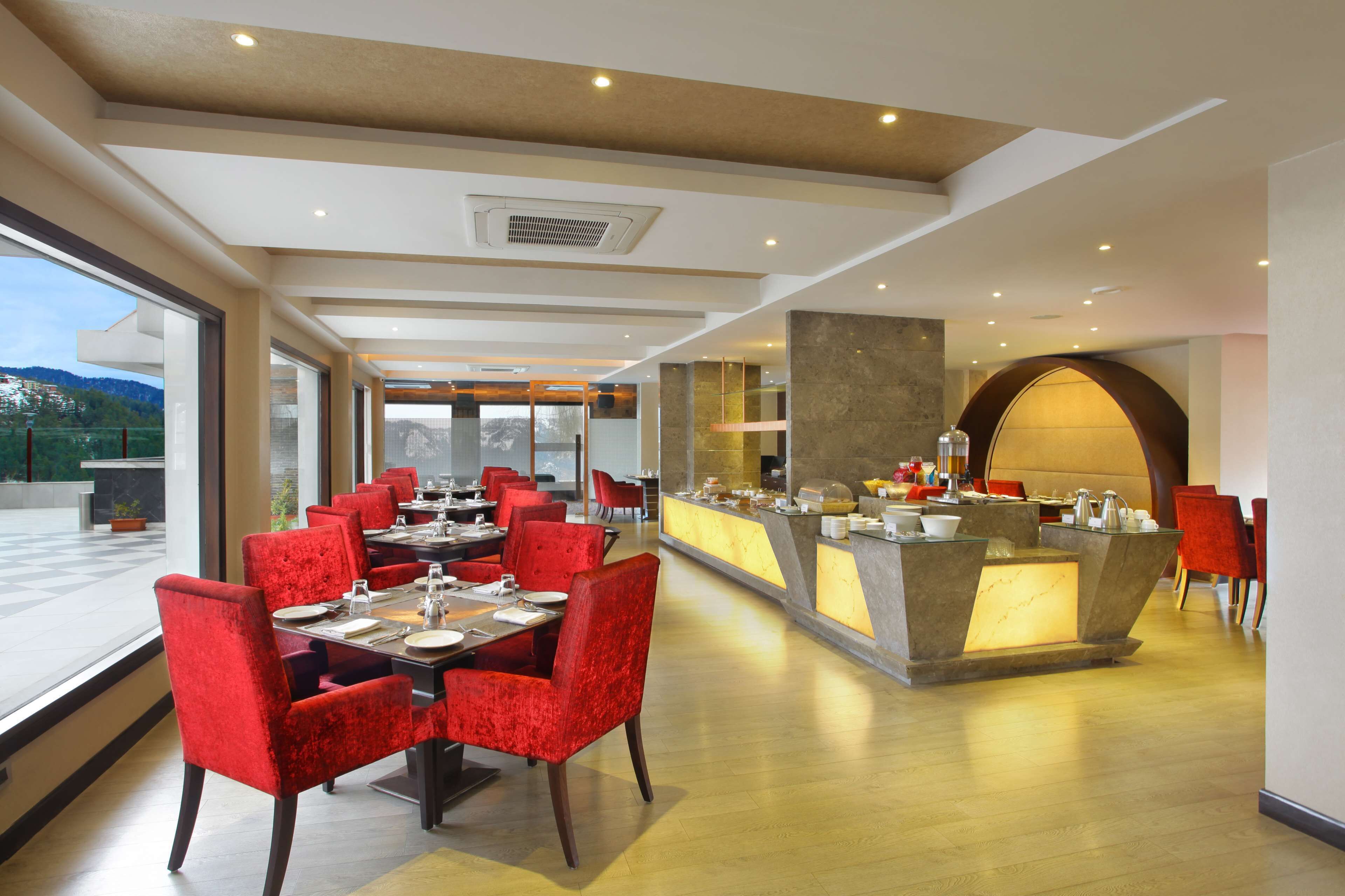 A modern restaurant with red upholstered chairs, a central island with a light-up display, and a view of the outdoors.
