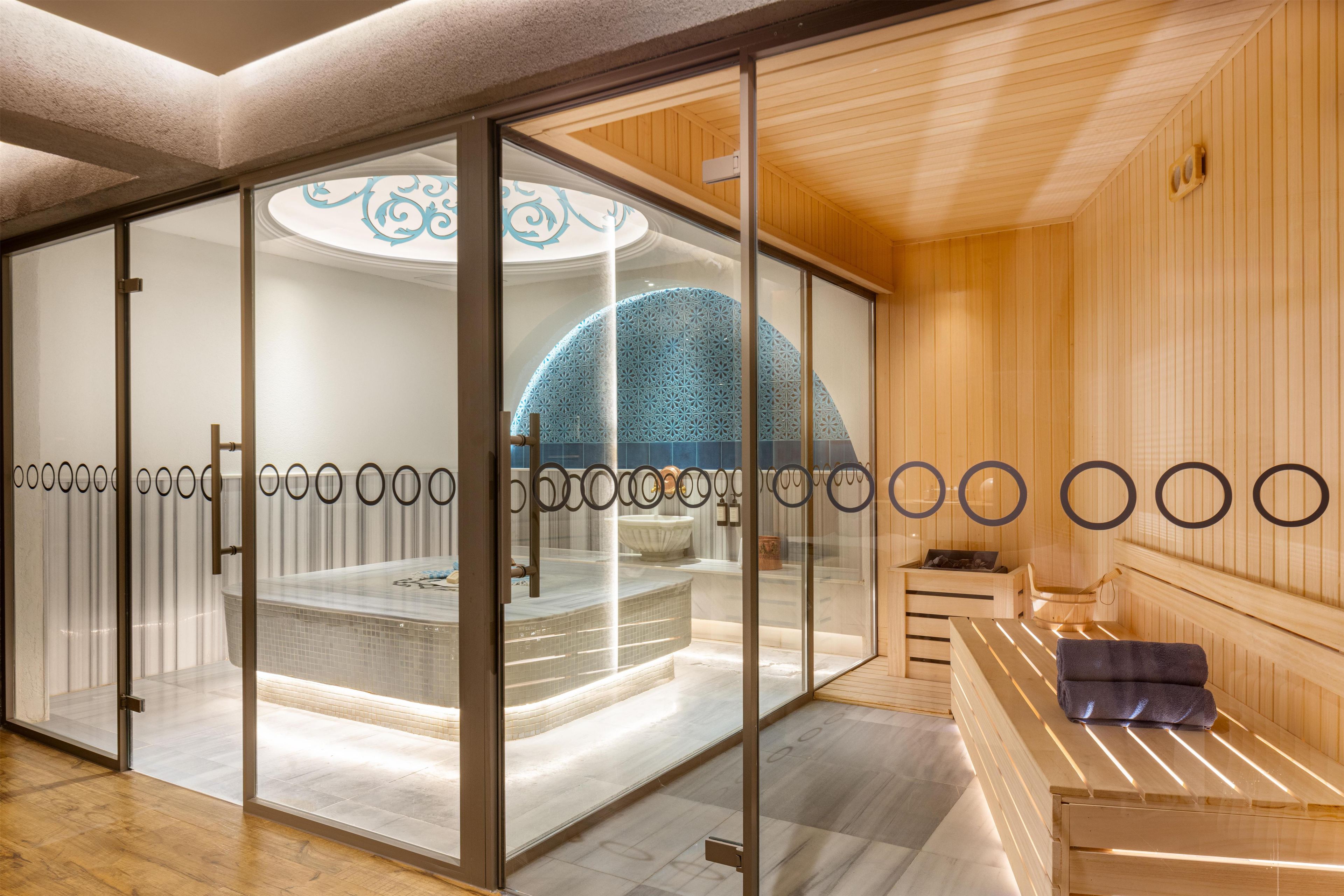 Un moderno spa con un mamparo de vidrio, una bañera de hidromasaje y una zona de sauna de madera.