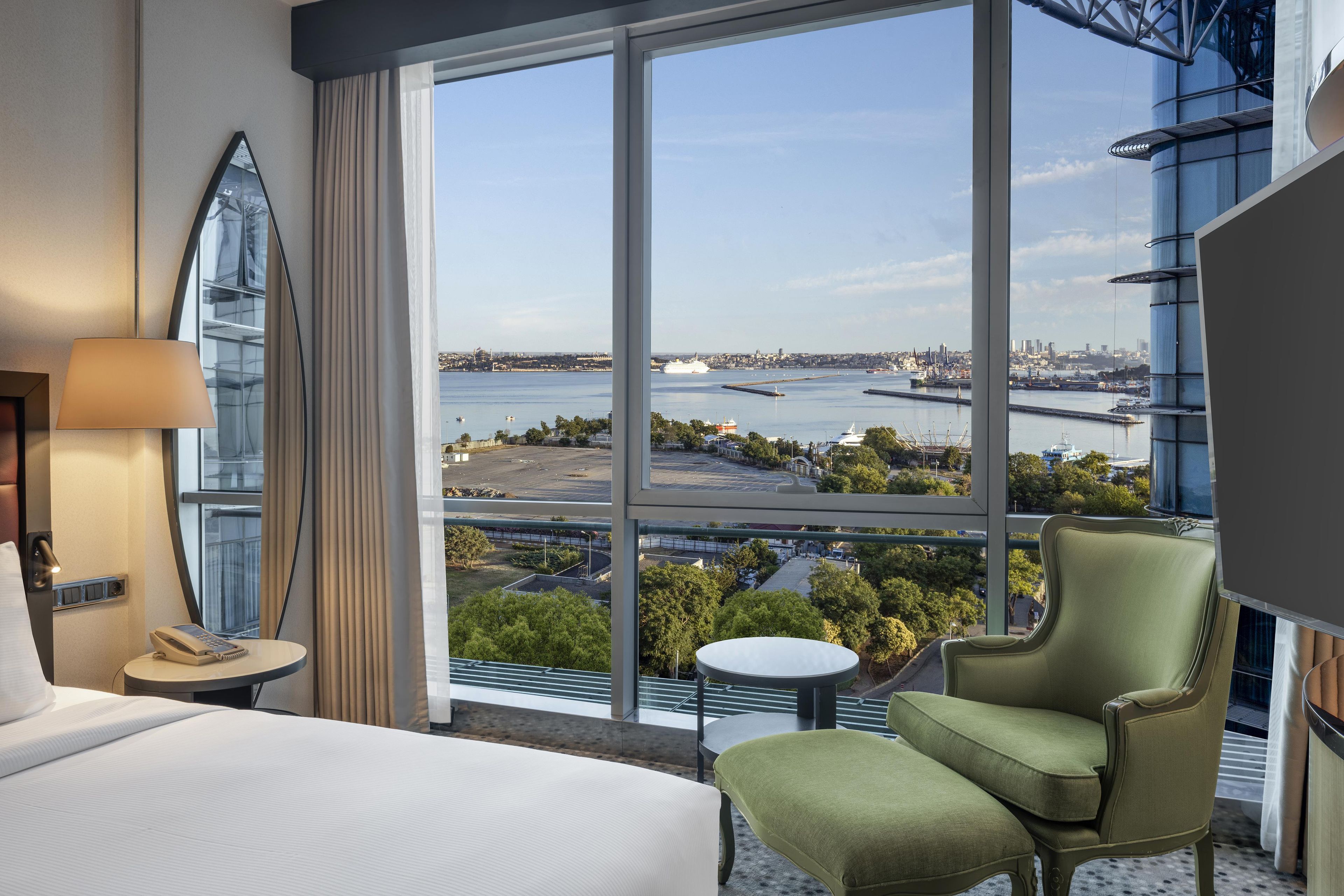 Habitación de hotel con un amplio ventanal que ofrece vistas a un río y al paisaje urbano.