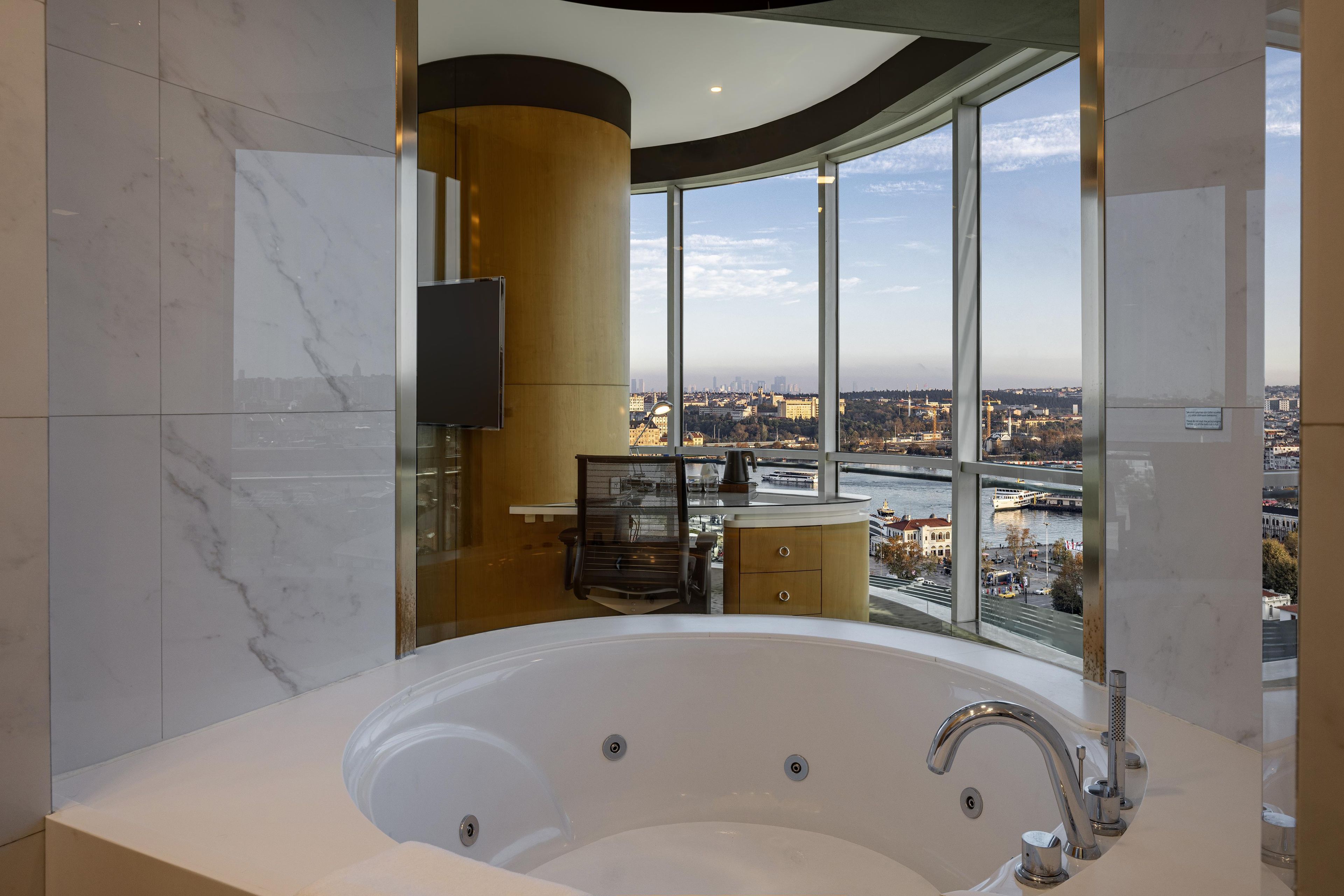 A modern bathroom with a large bathtub, a wooden vanity, and a city view through large windows.