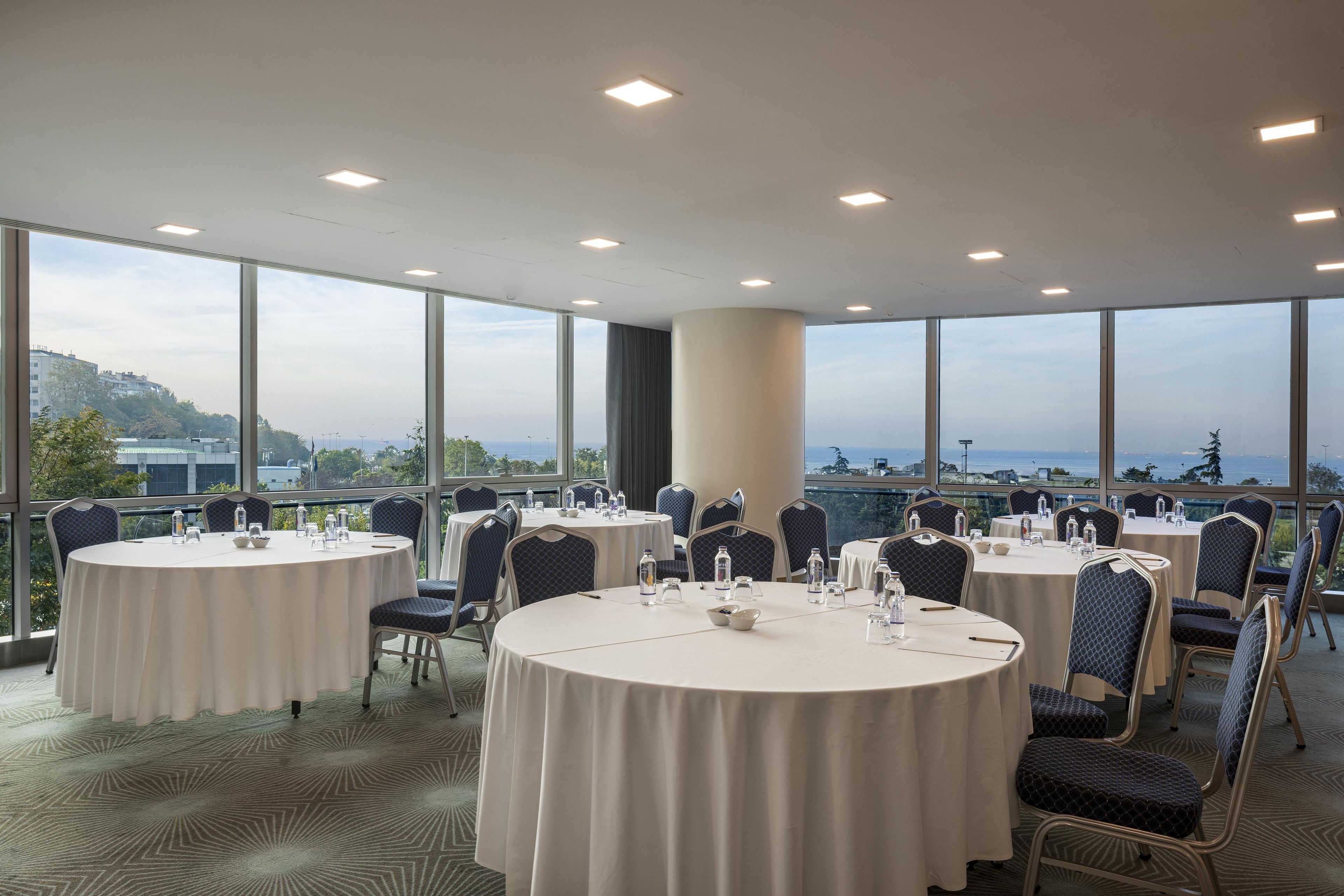 Una sala de conferències amb taules rodones, cadires i una vista panoràmica de la ciutat.