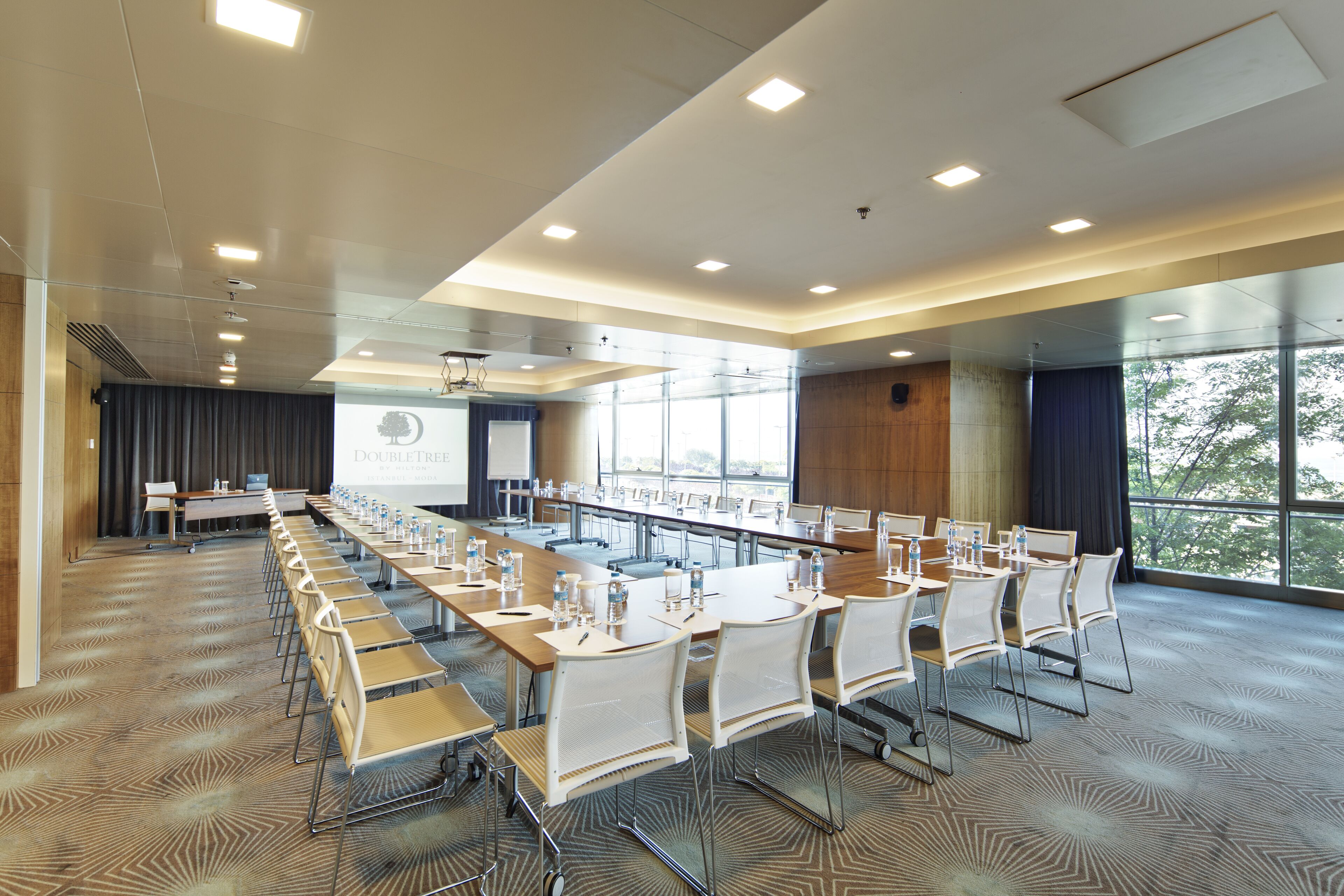 A conference room with a long table, chairs, and a projector screen.