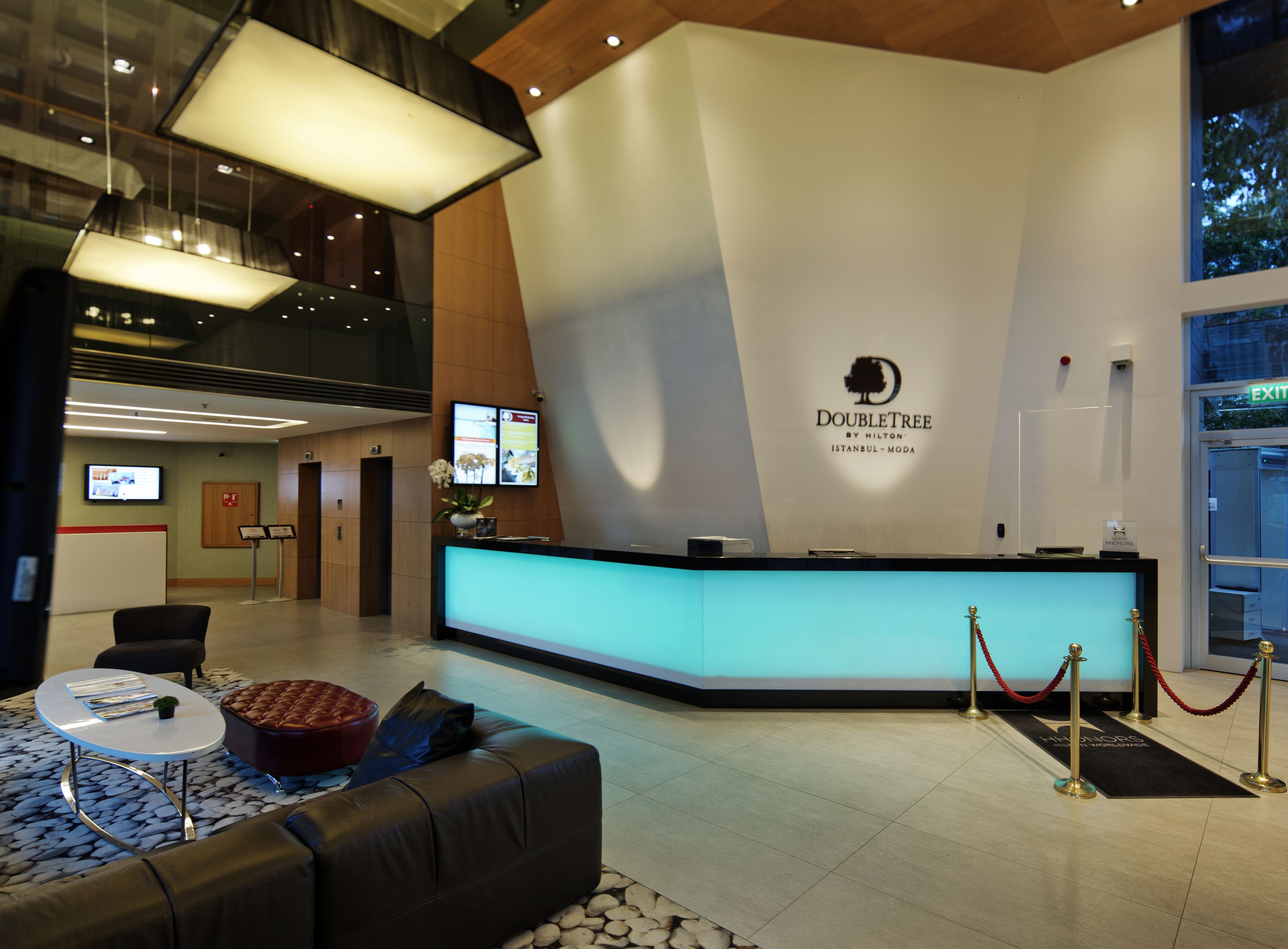 Zona de recepción de hotel con diseño moderno, que incluye un mostrador de recepción, un área de estar y un amplio ventanal con vistas al exterior.