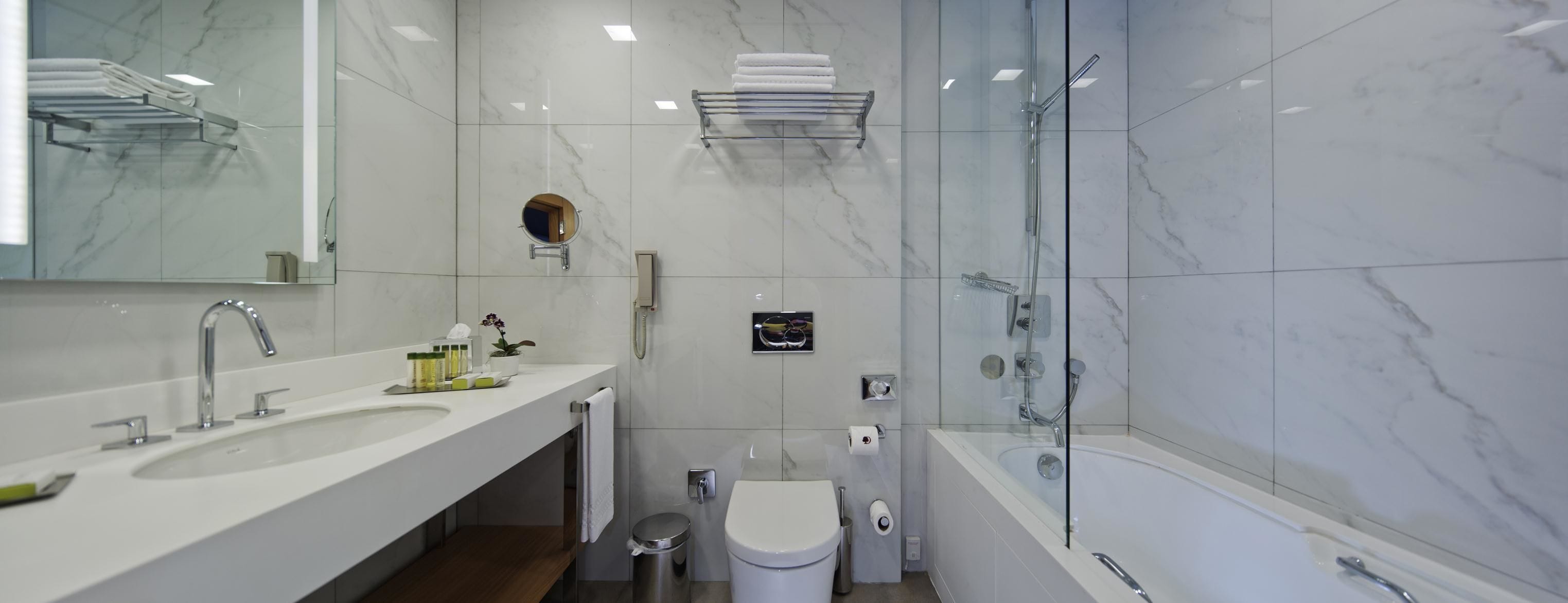 A modern bathroom with a large mirror, a sink with multiple faucets, a toilet, and a bathtub.