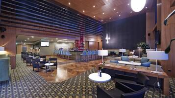 A spacious lobby with a high ceiling, a central seating area with sofas and chairs, a bar area, and a patterned floor.