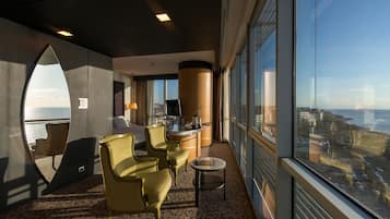 Una habitación de hotel moderna con un gran ventanal, una mesa redonda y dos sillones amarillos.
