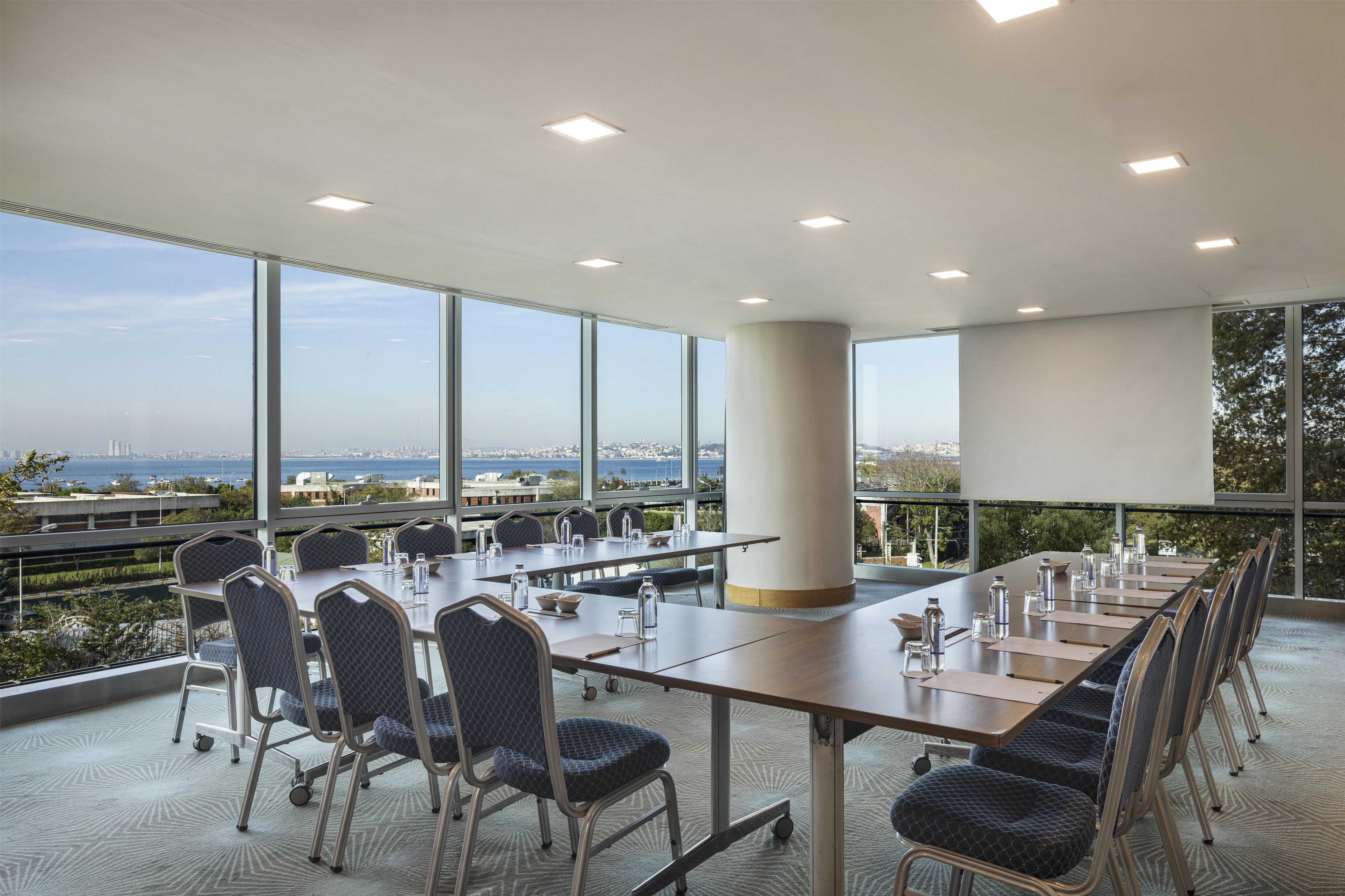 A conference room with a panoramic view, equipped with tables, chairs, and water bottles.