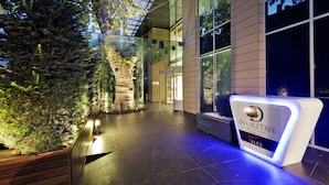 A modern hotel lobby with a glass ceiling, a large tree sculpture, and a reception desk labeled "DoubleTree by Hilton Istanbul Moda."
