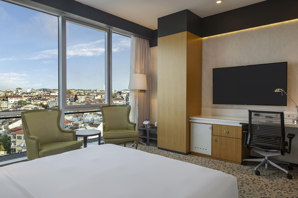 Una habitación de hotel con una cama grande, dos sillones, un escritorio, una silla y un televisor.