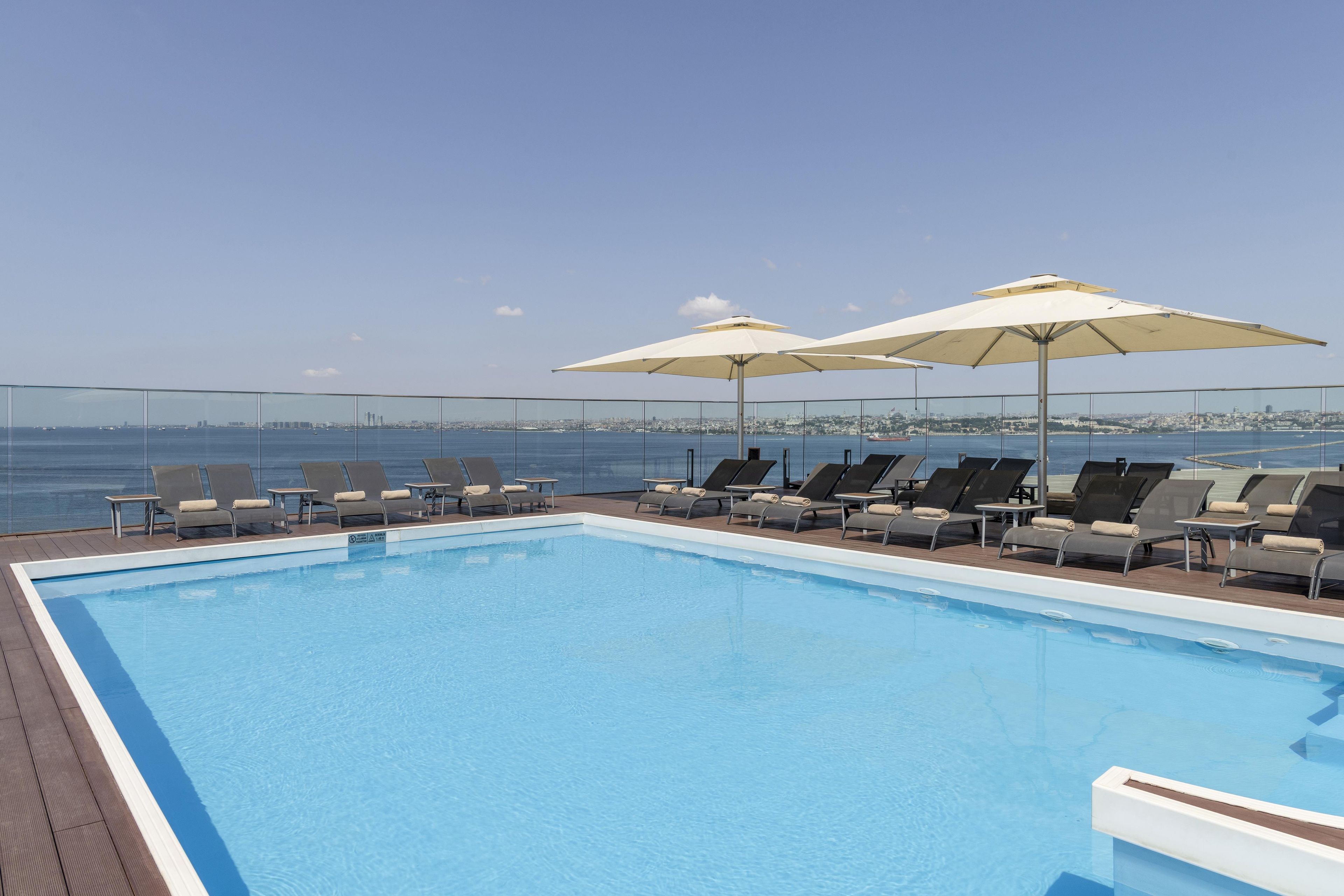 A pool with lounge chairs and umbrellas, overlooking a cityscape.