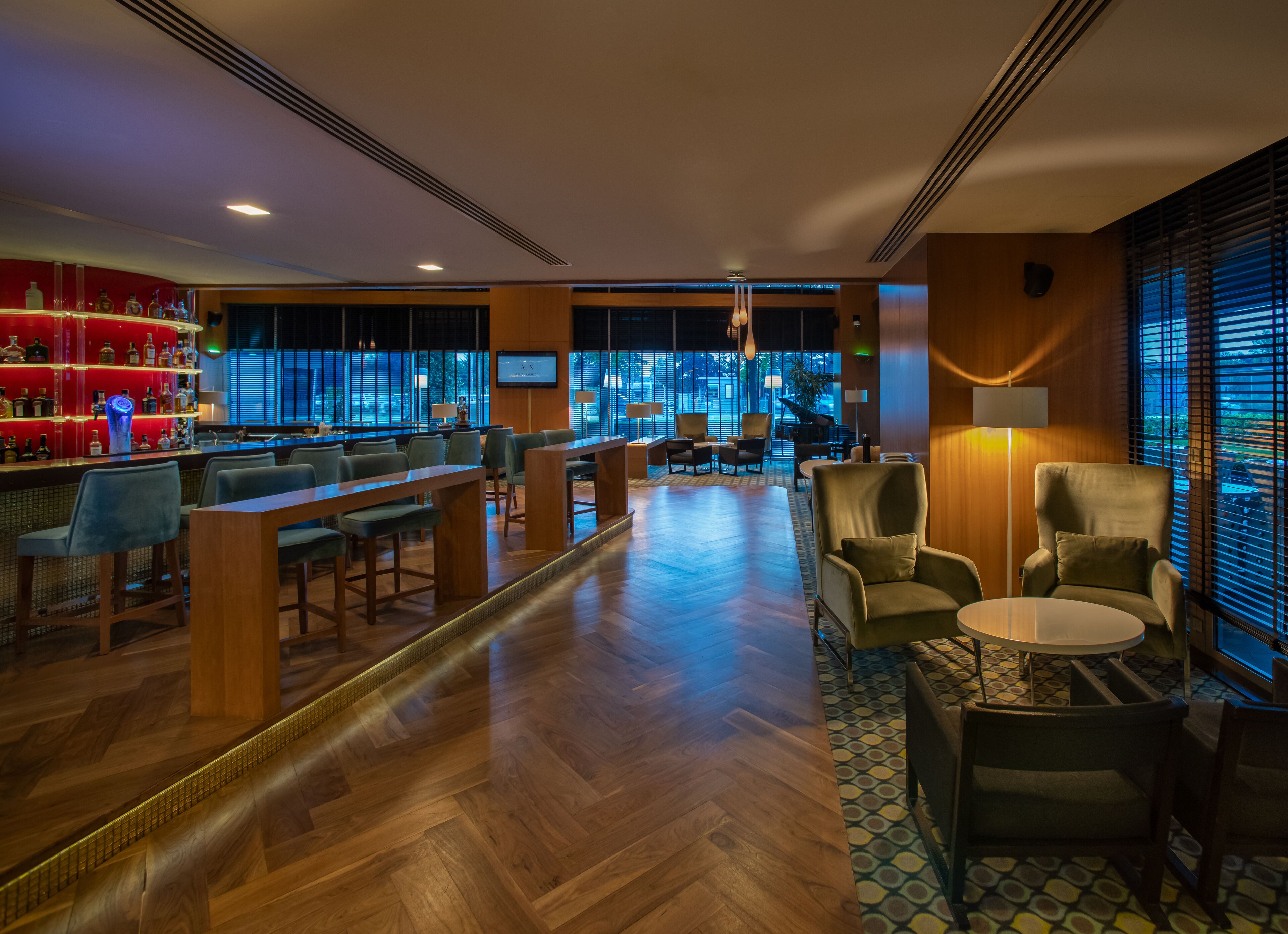 A bar area with wooden tables and chairs, a red liquor display, and a large window with blinds.