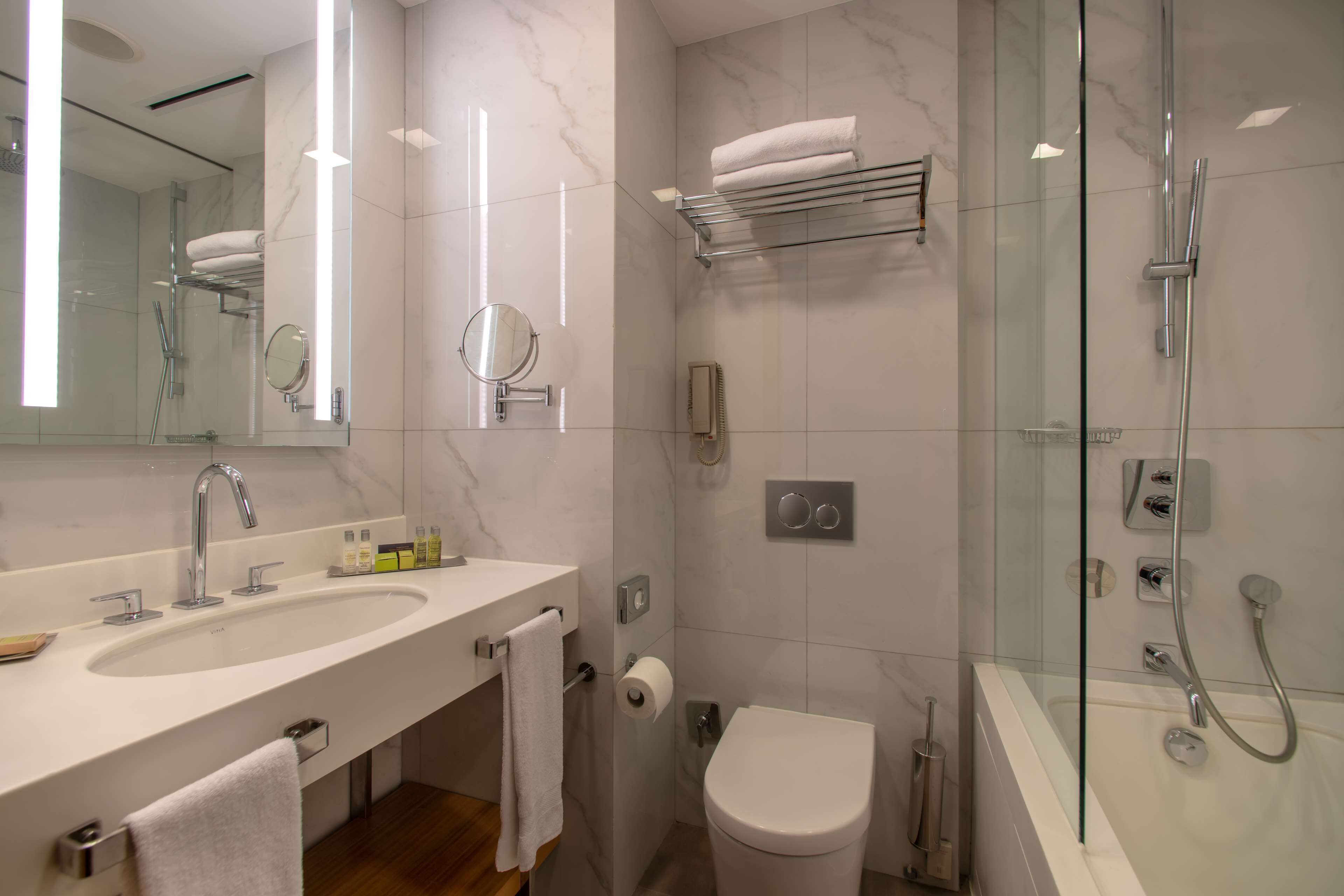 Un baño moderno con lavamanos grande, espejo, inodoro y zona de ducha con mampara de vidrio.