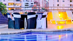 Área de piscina no terraço, com espreguiçadeiras e mesa para hóspedes.