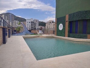 A swimming pool with a tiled deck, a lounge chair, and a building with a green wall and a sign.