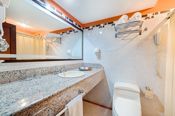 A bathroom with a granite countertop, a sink, a toilet, and a shower area. - Hotel Obelisco (Cali)