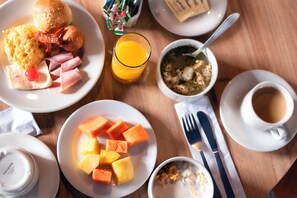 A breakfast setting with plates of eggs, ham, and fruit, a glass of orange juice, a bowl of soup, and a cup of coffee.