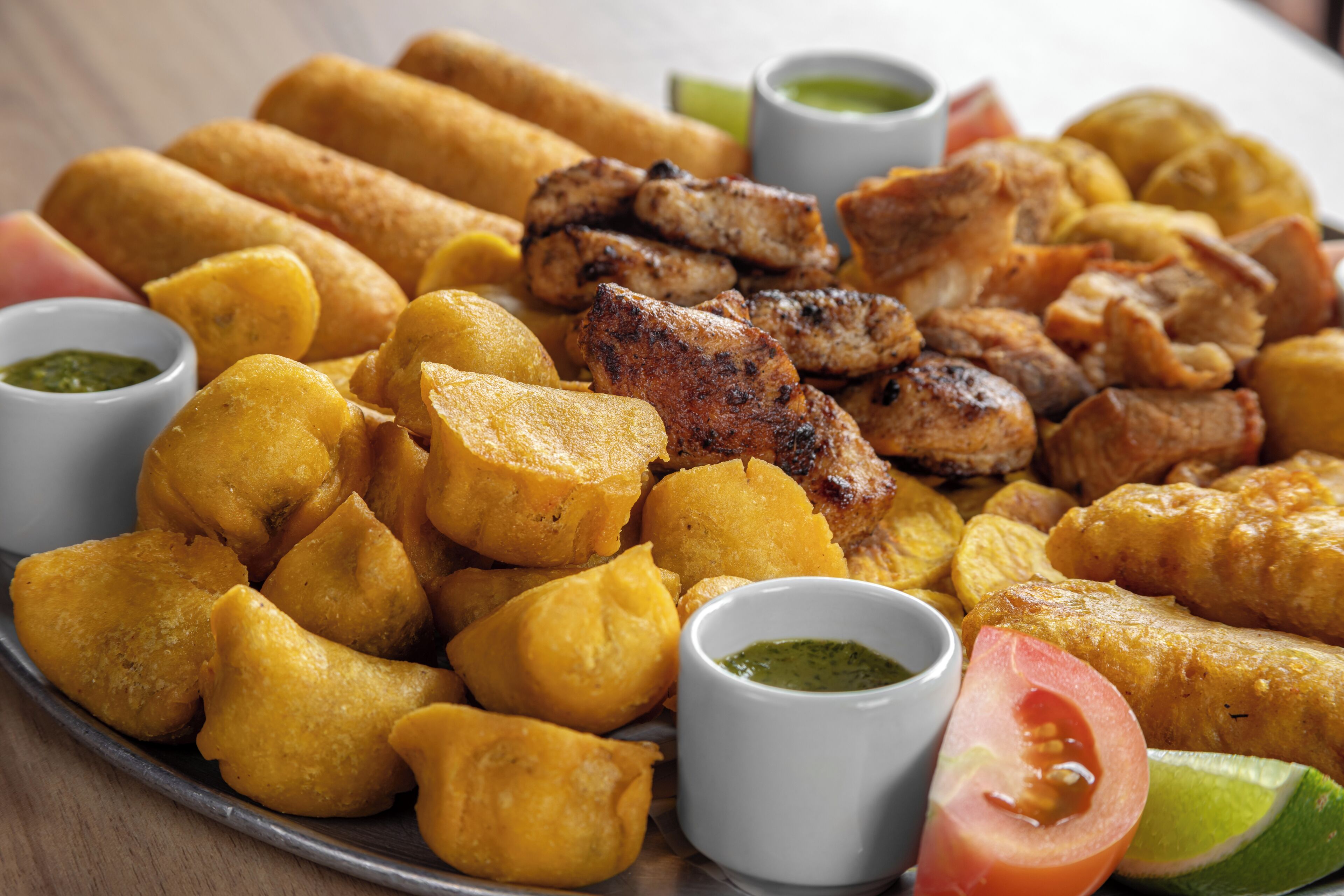 A plate of fried food including plantains, fried fish, and meat, accompanied by small bowls of dipping sauces.