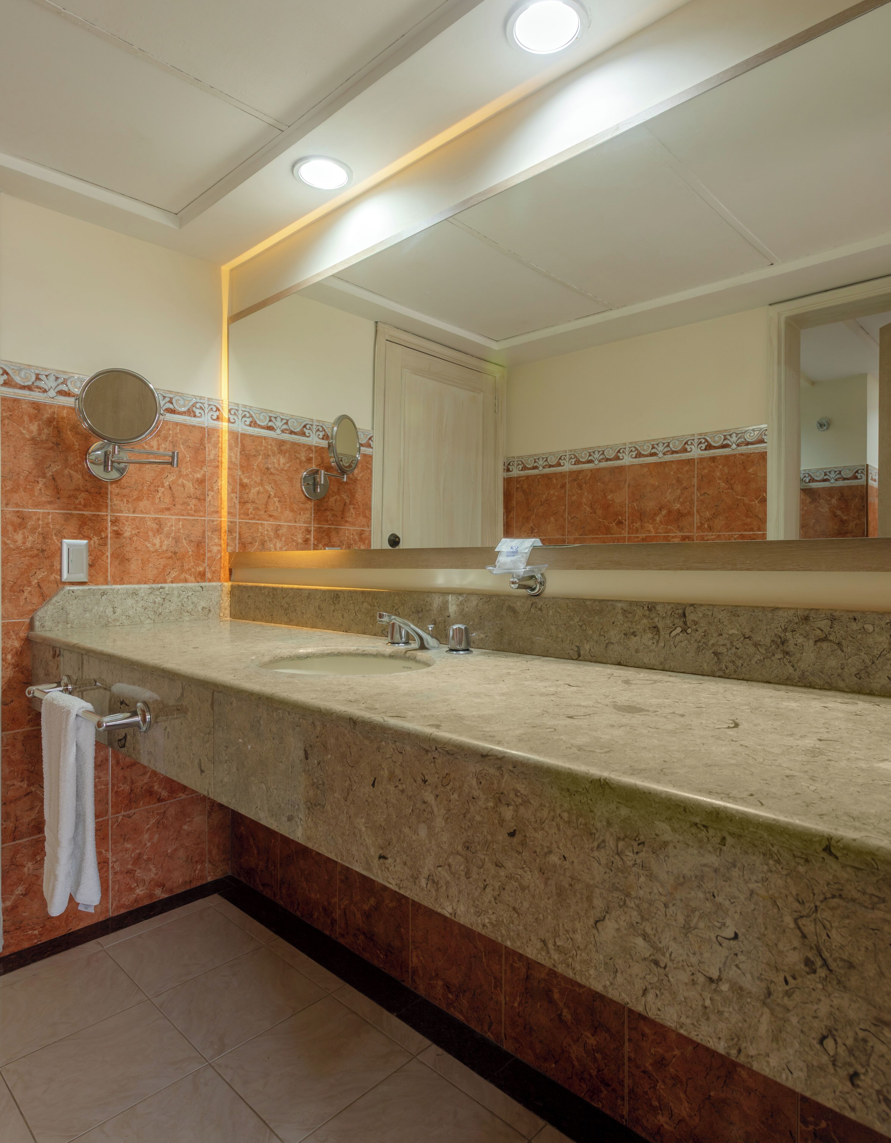 A bathroom with a marble sink, a mirror, and a towel rack.