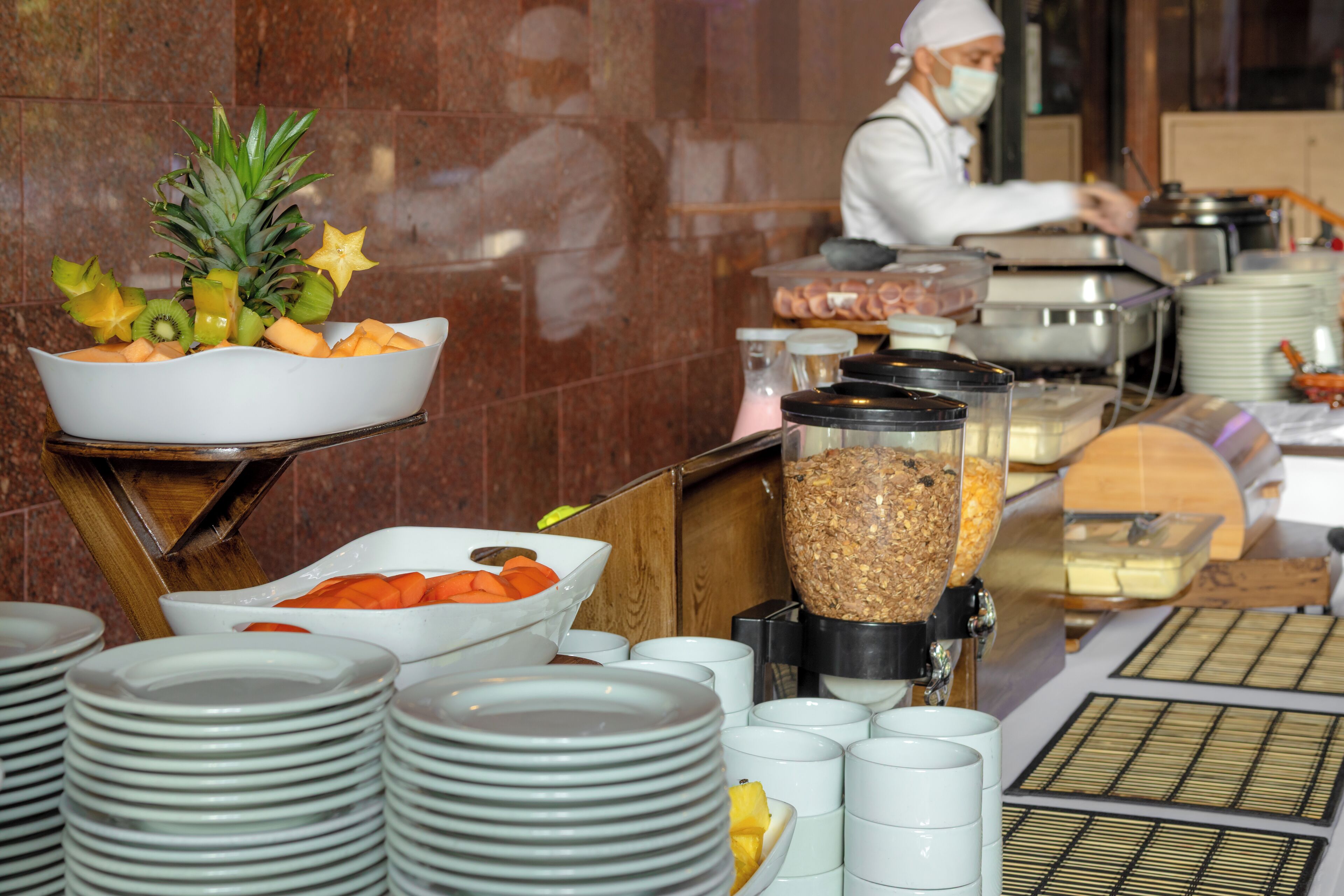 A buffet setup with various food items and a chef preparing food in the background.
