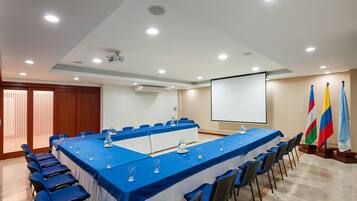 Una sala conferenze con un lungo tavolo, sedie, uno schermo per proiettore e bandiere.