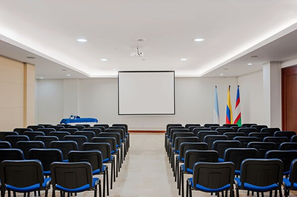 A conference room with rows of chairs, a projector screen, and flags. - Hotel Obelisco (Cali)