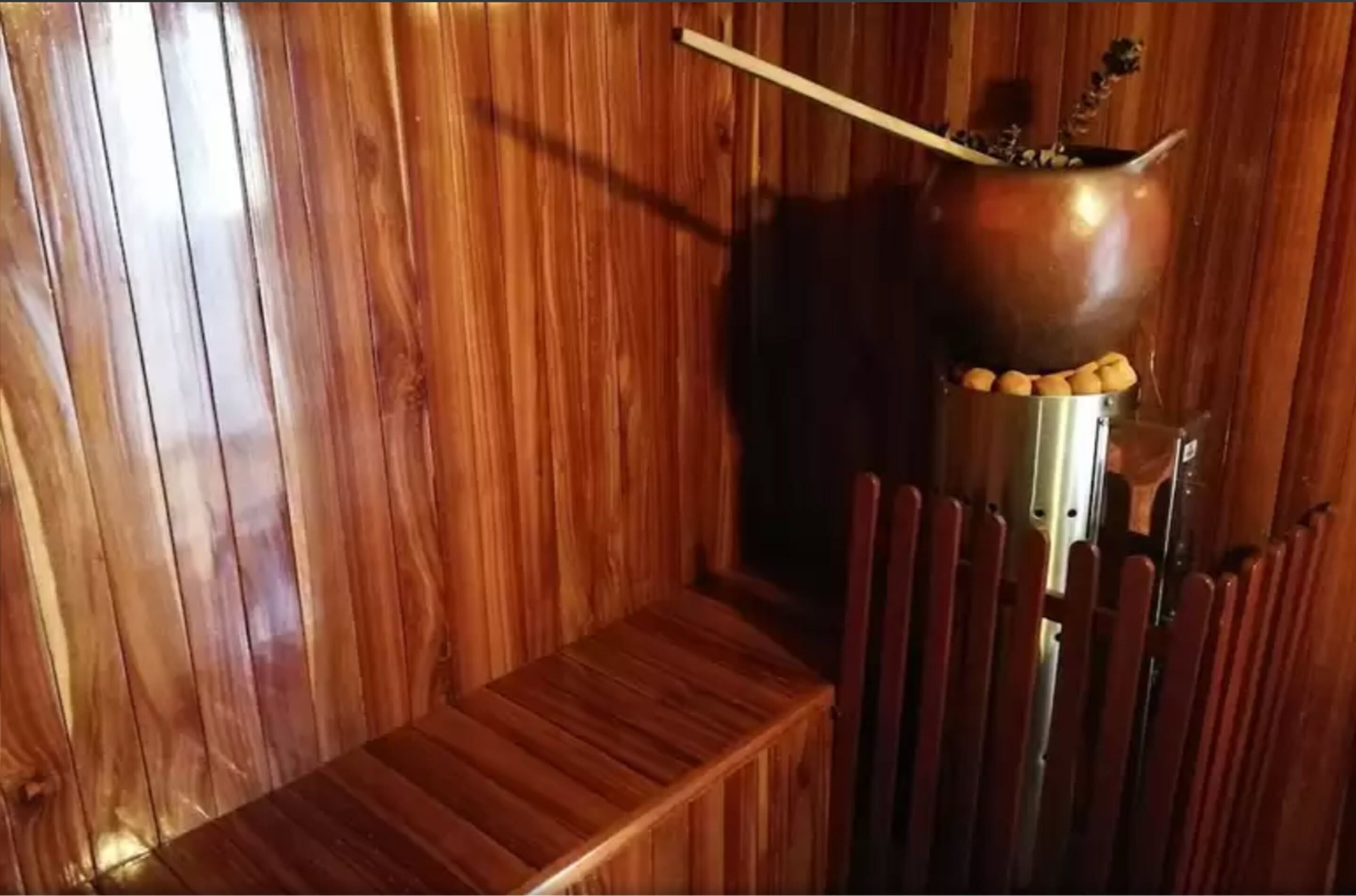 A wooden interior with a metal pot on a stand, a wooden bench, and a chair.