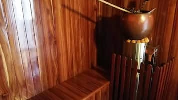 A wooden interior with a metal pot on a stand, a wooden bench, and a chair.