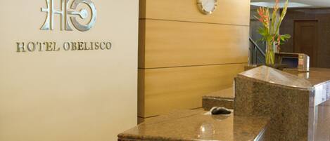 A reception desk with a clock and a sign for HOTEL OBELISCO.