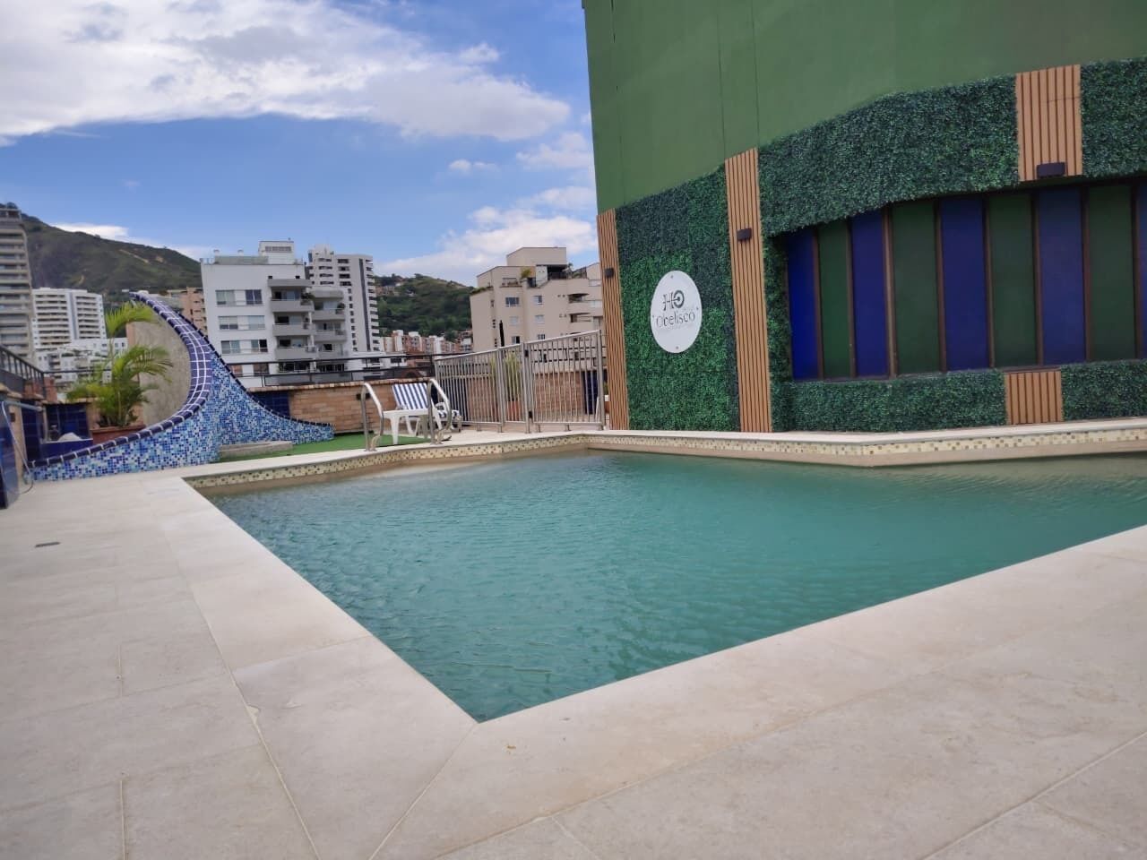 Una piscina con borde de azulejos, un muro verde con listones de madera verticales y un cartel con la inscripción 'nicelisco'.