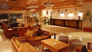 Un amplio vestíbulo con muebles de madera, un mostrador de recepción y una escalera que conduce a los pisos superiores.