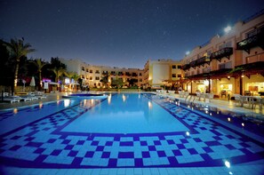 A swimming pool with a geometric tile pattern, surrounded by palm trees and buildings with balconies. - Falcon Naama Star Hotel (Sharm El Sheikh)