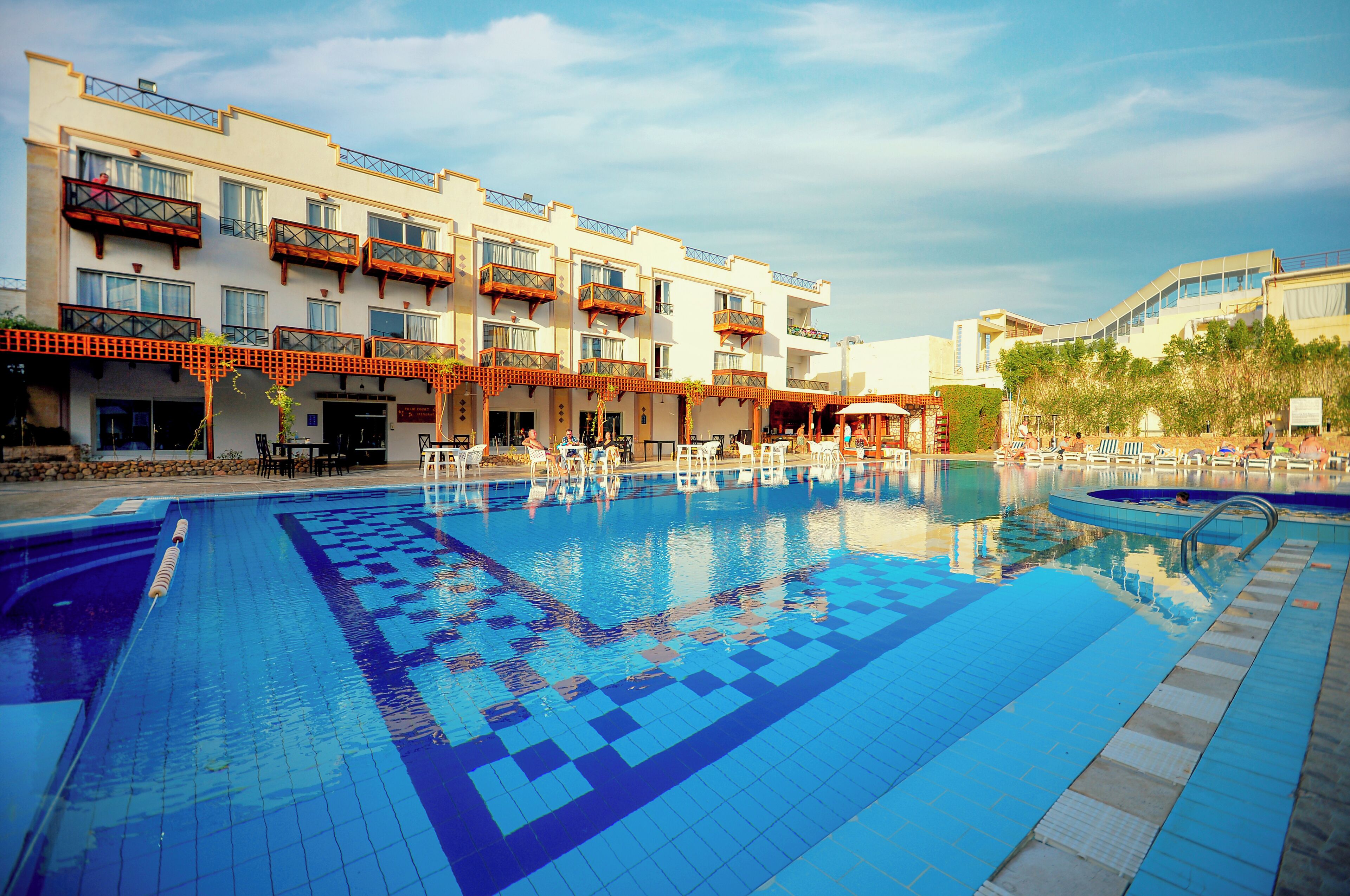 Un hotel con piscina, mobiliario exterior y un edificio de varios pisos con balcones.