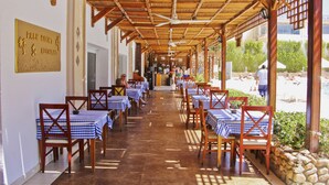 Un espacio de comedor al aire libre con techado, mesas y sillas, un cartel para el Restaurante Palm Court, y vistas del área de asientos al aire libre.
