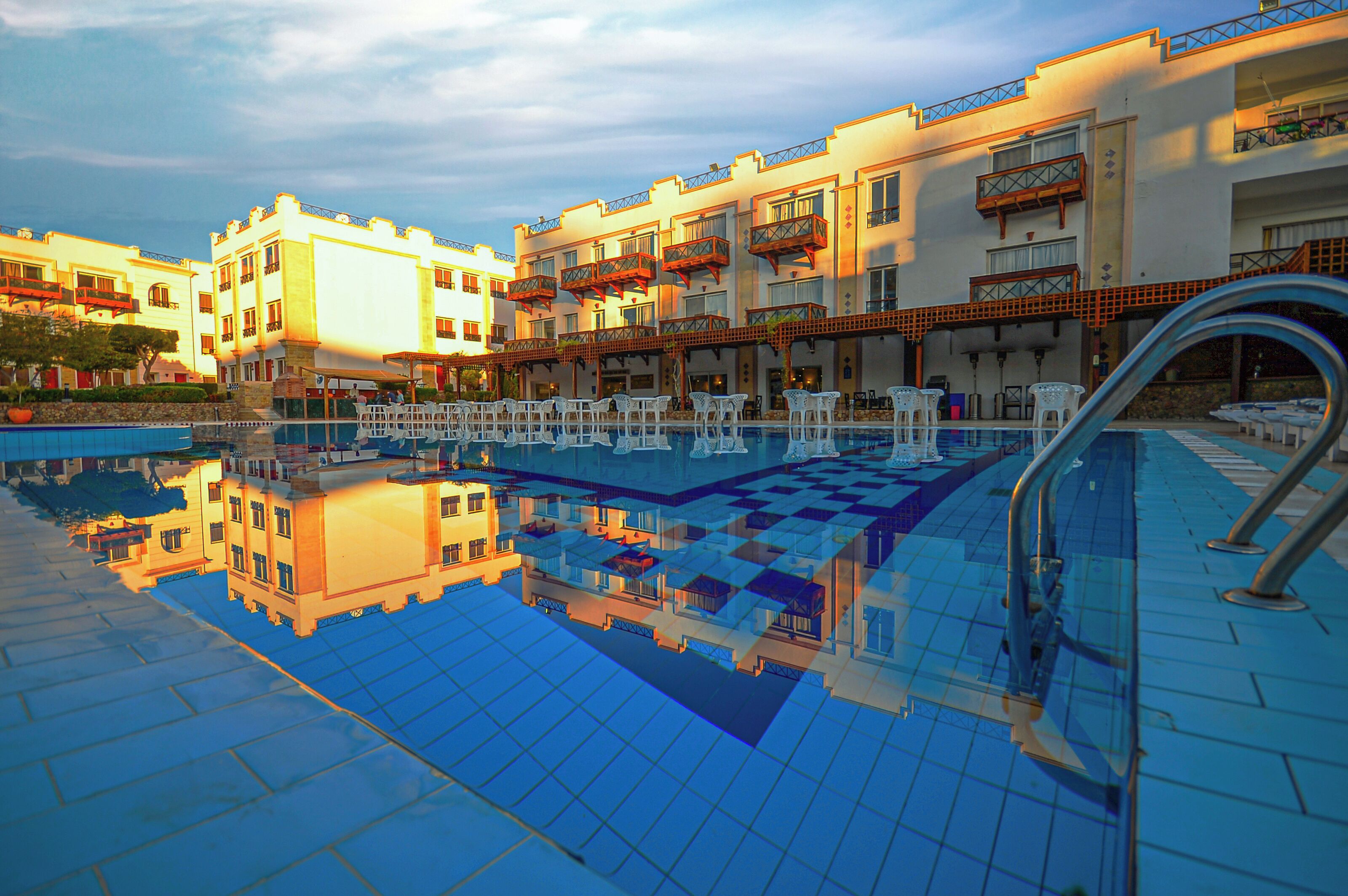 A hotel pool area with multiple levels of balconies, a clear pool, and a reflection of the buildings.