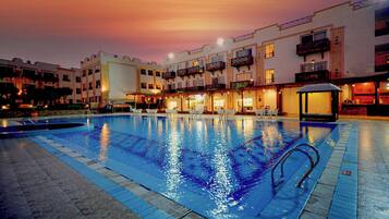 A swimming pool with a sunken area, surrounded by buildings with balconies and a covered seating area.