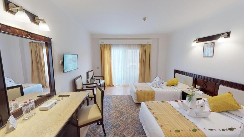 Een hotelkamer met twee bedden, een bureau, een stoel, een spiegel en een televisie.