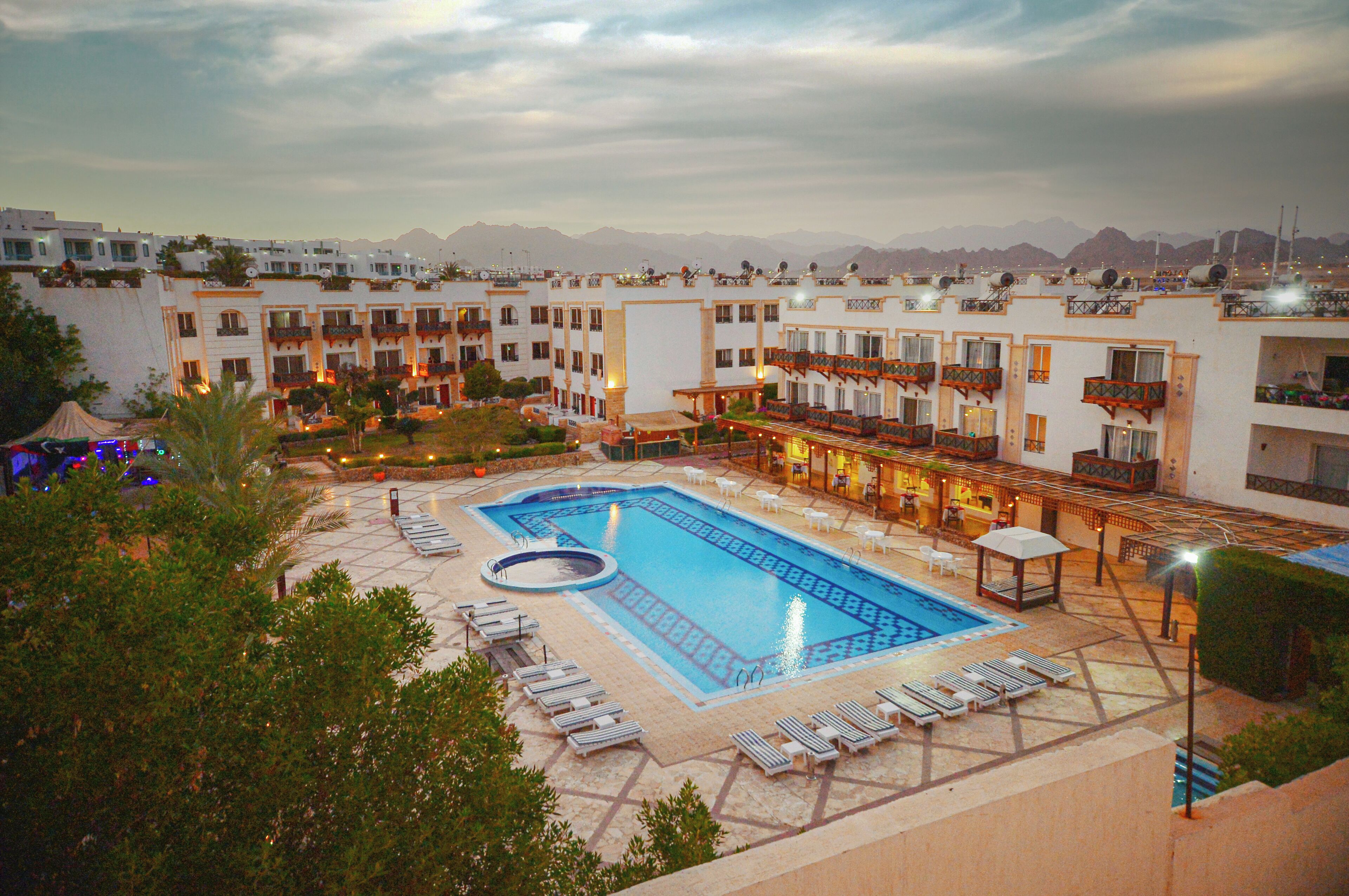 A hotel with a swimming pool, sun loungers, and a view of mountains.