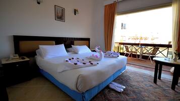 A hotel room with a large bed, a nightstand with a phone, a balcony with chairs and a table, and a patterned rug.