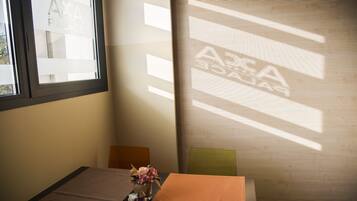 Ein Hotelzimmer mit Bett, einem kleinen Tisch mit Blumenvase, einem Fenster und einer Projektionsleinwand, die den Namen des Hotels zeigt.