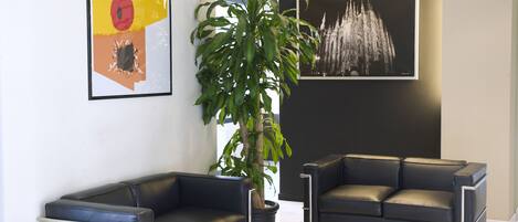 A modern living room with two black leather sofas, a coffee table, a potted plant, and artwork on the walls.