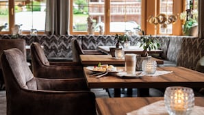 A restaurant with wooden tables and cushioned chairs, a view of the outdoors, and a candle on the table. - Hotel Alpenjuwel Jäger (Tux)