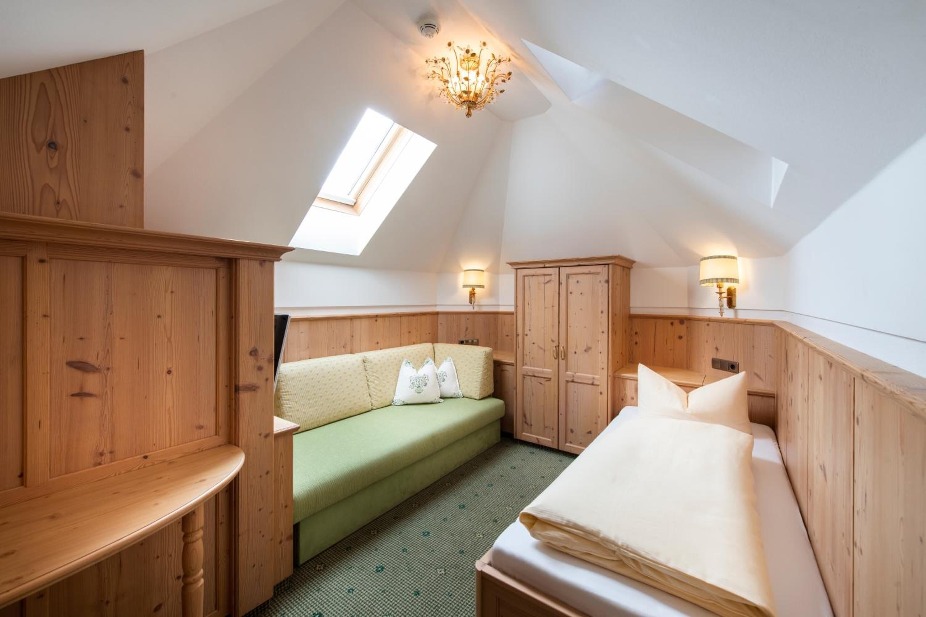A cozy attic bedroom with a sloped ceiling, wooden walls, a green sofa, a bed, and a skylight.