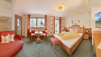 A hotel room with a bed, a sofa, a dining table with chairs, a TV, and a window with curtains.