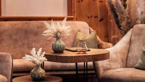 A cozy living room with a sofa, two round tables, a vase, and a painting on the wall. - Hotel Alpenjuwel Jäger (Tux)