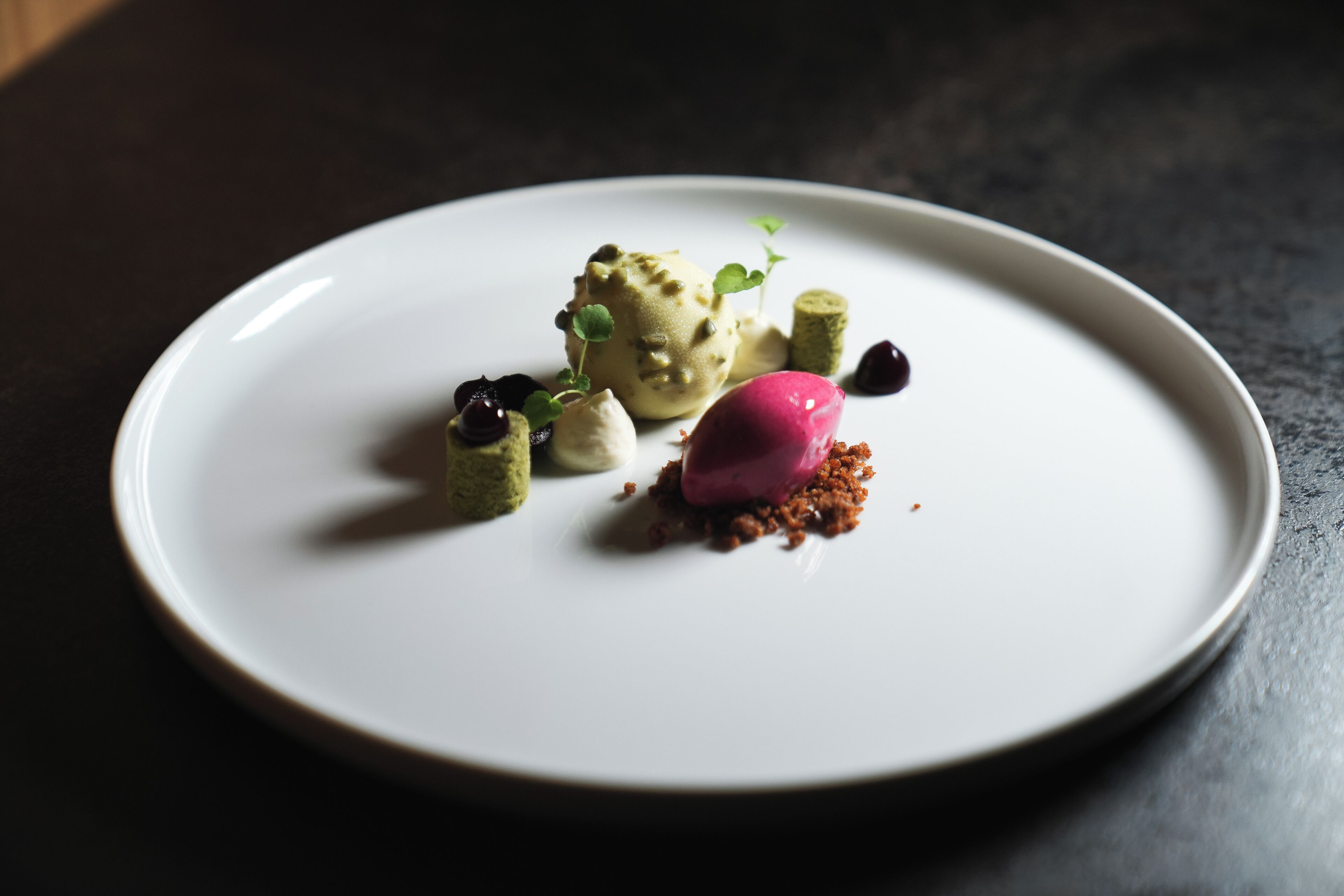 Un plato blanco con un postre de helado, bayas y crumble.