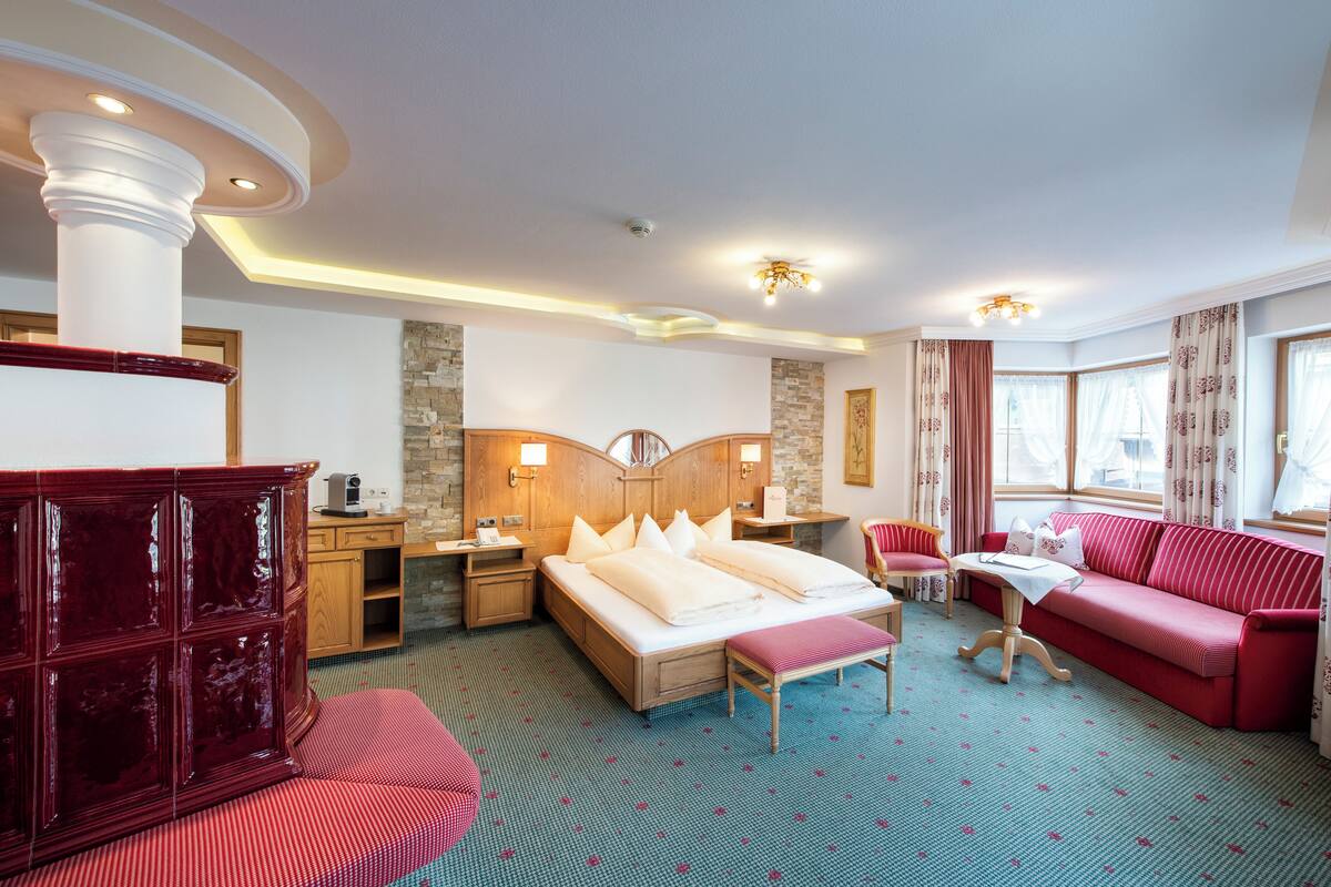 Ein Hotelzimmer mit einem großen Bett, einem roten Sofa, einem Holzkasten, einem Schreibtisch mit Lampe und einem Fenster mit Vorhängen.